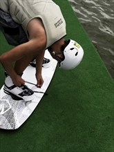 Young man with helmet and wakeboard, tying shoes in front of jump start, water sports