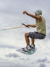 Young man jumping with wakeboard, water sports, water skiing in wakepark