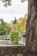 A horse statue on a pedestal surrounded by autumnal trees and urban surroundings, Kirchheim Teck,