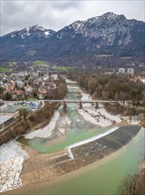 View of a river flowing through a town with a bridge, surrounded by snow-capped mountains and