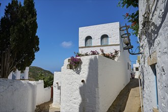 White, Mediterranean houses with blue sky, flowers on the balcony, sunny narrow alley, Chora, main