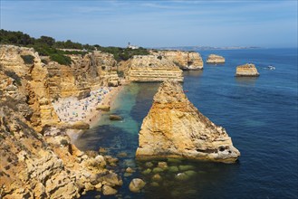 A beautiful beach on a rocky coast with clear blue water and sunny skies, Praia da Marinha, Lagoa,