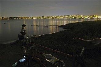 Night view of a lake with illuminated city in the background, bicycle in the foreground, Tönsberg,