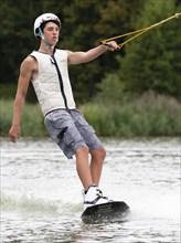 Sporty young man with helmet and waistcoat on wakeboard in lake, water sports, water skiing in