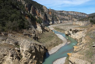 A clear river flows through a rocky gorge between overgrown mountains under a blue sky, Noguera