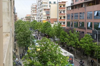 Looking down on treelined street vehicles traffic cars taxis buses in city centre of Tirana,