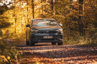 Vehicle on forest path in autumn with orange leaves, electric car VW ID5, Gechingen, Black Forest,