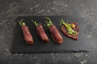 Slices of smoked salted meat with green pea microgreen on black concrete background. Side view,