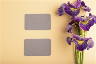 Gray business card with lilac iris flowers on orange pastel background. top view, flat lay, copy