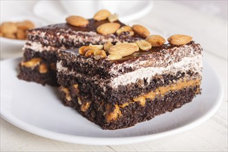 Chocolate cake with caramel, peanuts and almonds on a white wooden background. cup of coffee, top