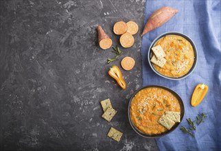 Sweet potato or batata cream soup with sesame seeds and snacks in blue ceramic bowls on a black