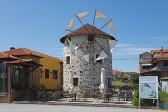 A converted windmill into a restaurant with outdoor seating under a clear blue sky, Ierissos,