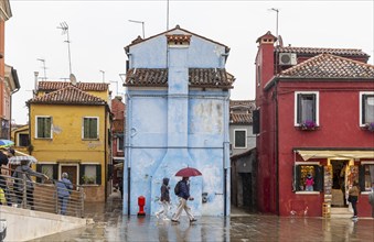 City view of Burano with colourfully painted houses and canals. Rainy weather, people are carrying