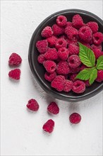 Fresh raspberries, on a black plate, with leaves, top view, on a white table