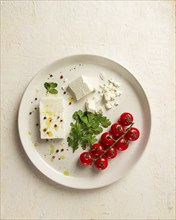 Feta cheese, for salads, with cherry, green butter, greens, on a white plate, appetizer, top view,