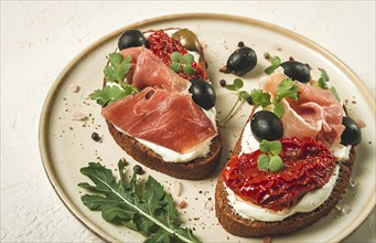 Sandwiches with cheese and prosciutto, dried tomatoes and olives, breakfast on a plate