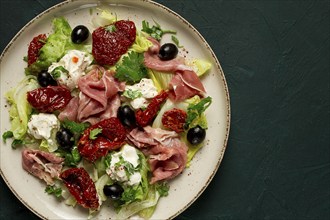 Salad with dried tomatoes, prosciutto, soft cheese, olives, homemade, top view