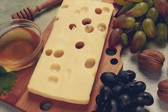 Cheese with big holes, emmental, maasdam, brie cheese, on a cutting board, with grapes and honey,