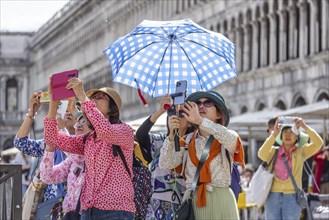 Tourists from Asia with mobile phones and parasols taking photos. Souvenir photo of St Mark's