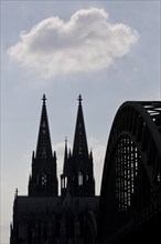 The towers of Cologne Cathedral and the Hohenzollern Bridge as a silhouette with a cloud, Cologne,