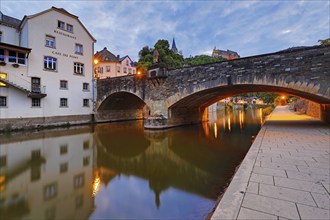 Town view of Vianden with the old stone bridge over the river Our and the castle in the evening,