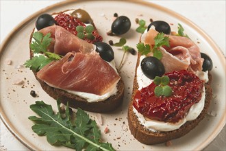 Sandwiches with cheese and prosciutto, dried tomatoes and olives, breakfast on a plate