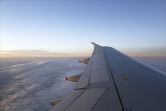 View out of the aircraft window onto the wing and the clouds during sunrise