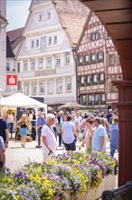 Market scene in front of a half-timbered house and a pharmacy, animated by people and decorated