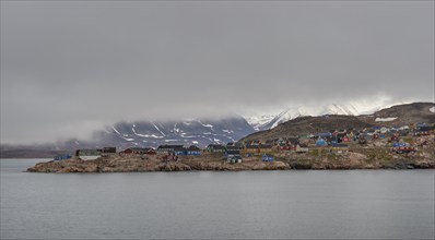 Colourful houses, secluded Arctic Inuit settlement, cloudy coastal landscape against a mountain