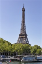 The Eiffel Tower in the centre of Paris with boats on the river and green trees, Paris