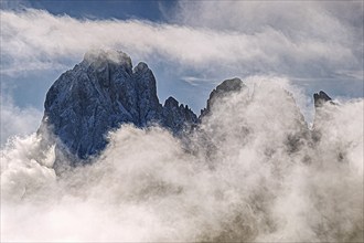 Impressive snow-covered mountain peak, partly covered by clouds, under a clear sky, Val Gardena,