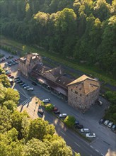 Aerial view of an old railway station building on a street with parked cars, surrounded by a green