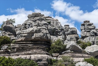 Massive rock formations under a blue sky with white clouds and green vegetation, karst mountains,