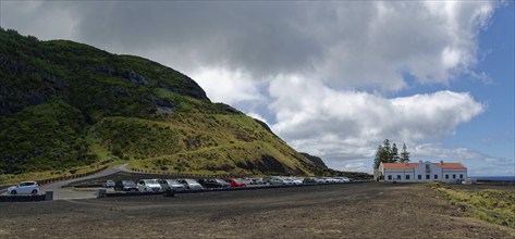 Car park with many cars next to a white house and thermal bath in a lava landscape under a cloudy