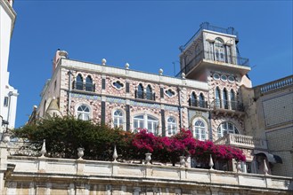 A multi-storey historic building with a balustrade decorated with flowers and a colourful façade,