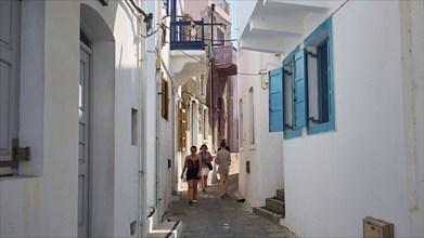 Narrow alley with white walls and colourful shutters, strollers in summer, Mandraki, Nisyros,