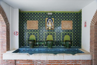 A decorated interior with blue mosaic and several taps, adorned with religious symbols and Spanish