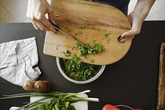 Overhead view of pouring cilantro from wooden cutting board into a bowl with stuffing