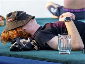 Young man exhausted sleeps off, empty glass, hat over his head