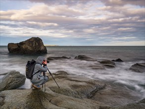 Photographer with tripod on smooth rocks by the sea, Utakleiv, Vestvågøya, Lofoten, Norway, Europe