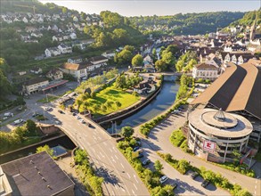 Aerial view of a shopping centre and a bridge over a canal in a green town with a hilly landscape,