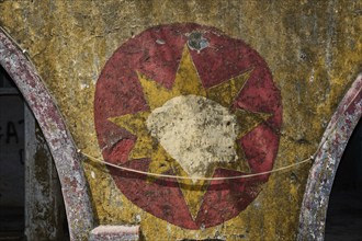 Worn mural of a star symbol with faded red and yellow tones, surrounded by peeling old plaster and