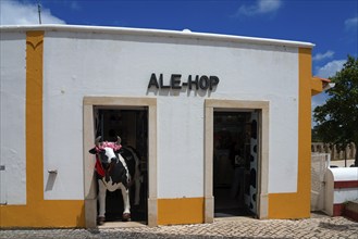 Shop front with eye-catching plastic cow decoration under a blue sky, Óbidos, Obidos, Oeste,