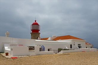 A white building with a red lighthouse under a cloudy sky, Cape St Vincent, Cape St Vincent, Cabo