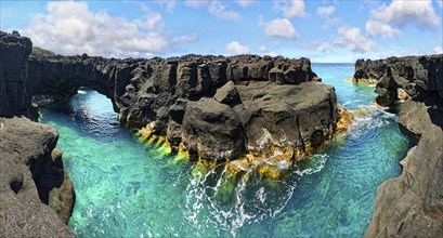 Rugged lava rock formations with a natural arch over a turquoise sea under a blue sky, A Porta do