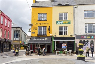 Colourful houses in a lively pedestrian zone with restaurants and cafés, people sitting outside,