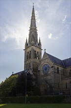 Tall Gothic church tower rising into the sky with surrounding trees and buildings, Letterkenny