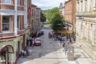 Lively pedestrianised area with cafés and shops, lined with red brick buildings and trees,