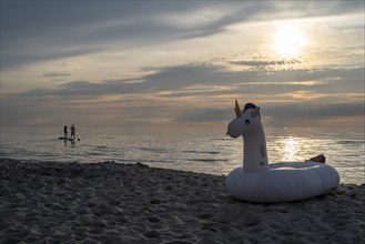 An inflatable unicorn on the beach at sunset, two people paddling in the calm sea, Baltic Sea