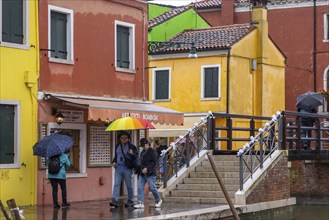 City view of Burano with colourfully painted houses and canals. Rainy weather, people are carrying